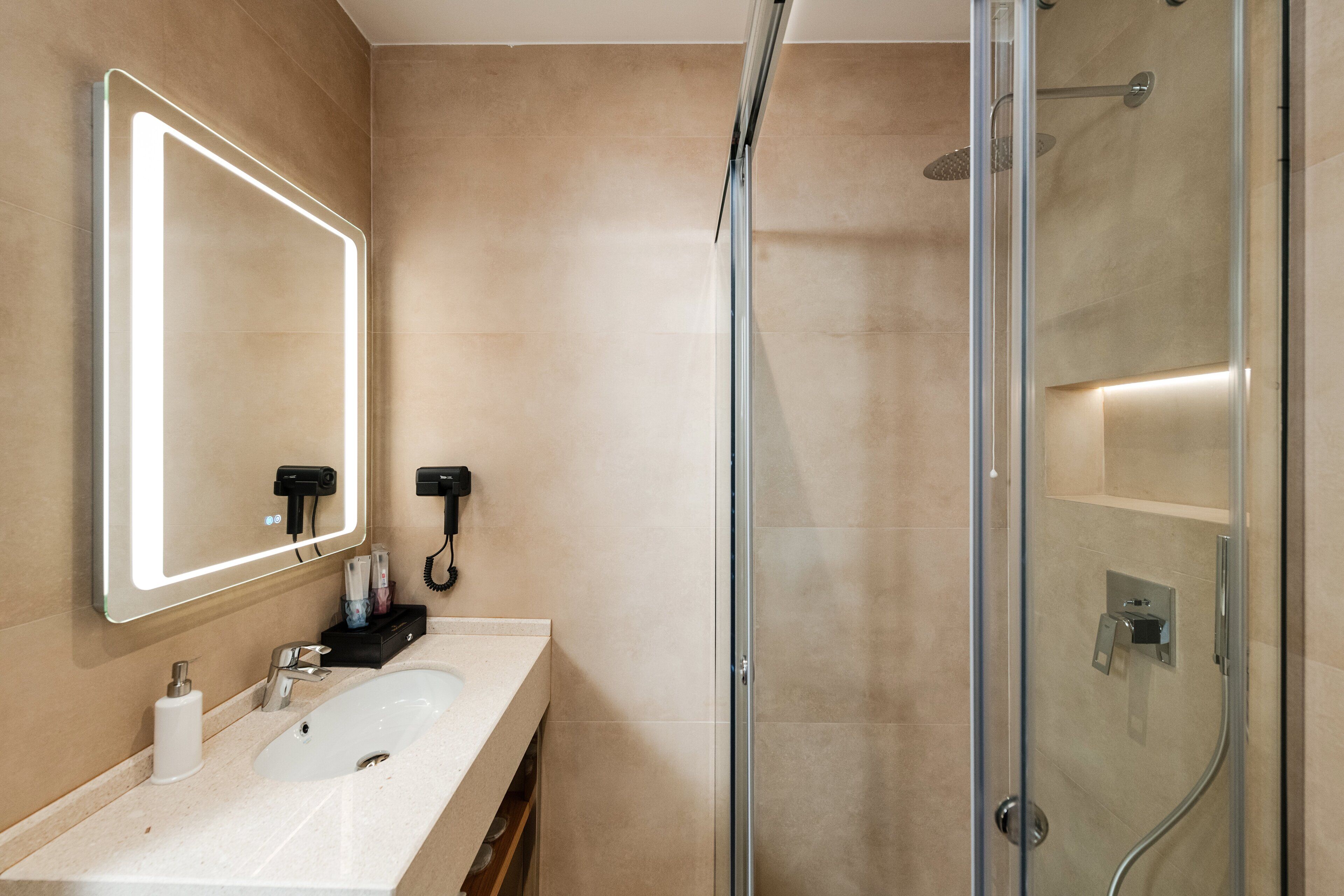 Ein modernes Badezimmer mit einem großen Spiegel, zwei Waschbecken, einer Duschkabine aus Glas und einem Handtuchhalter.