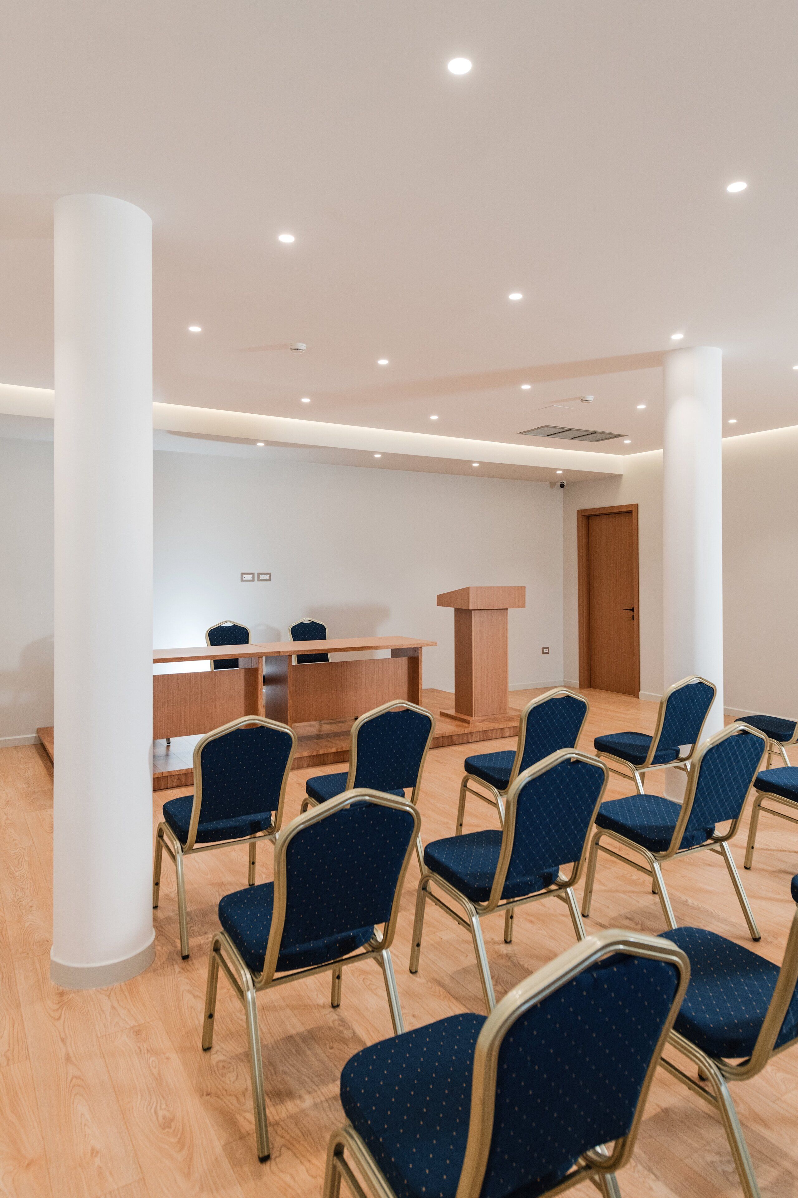 A conference room with rows of blue chairs, a wooden podium, and a white pillar.