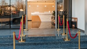 Entrada de un hotel con mostrador de recepción, fachada de vidrio y alfombra roja que conduce a la entrada.