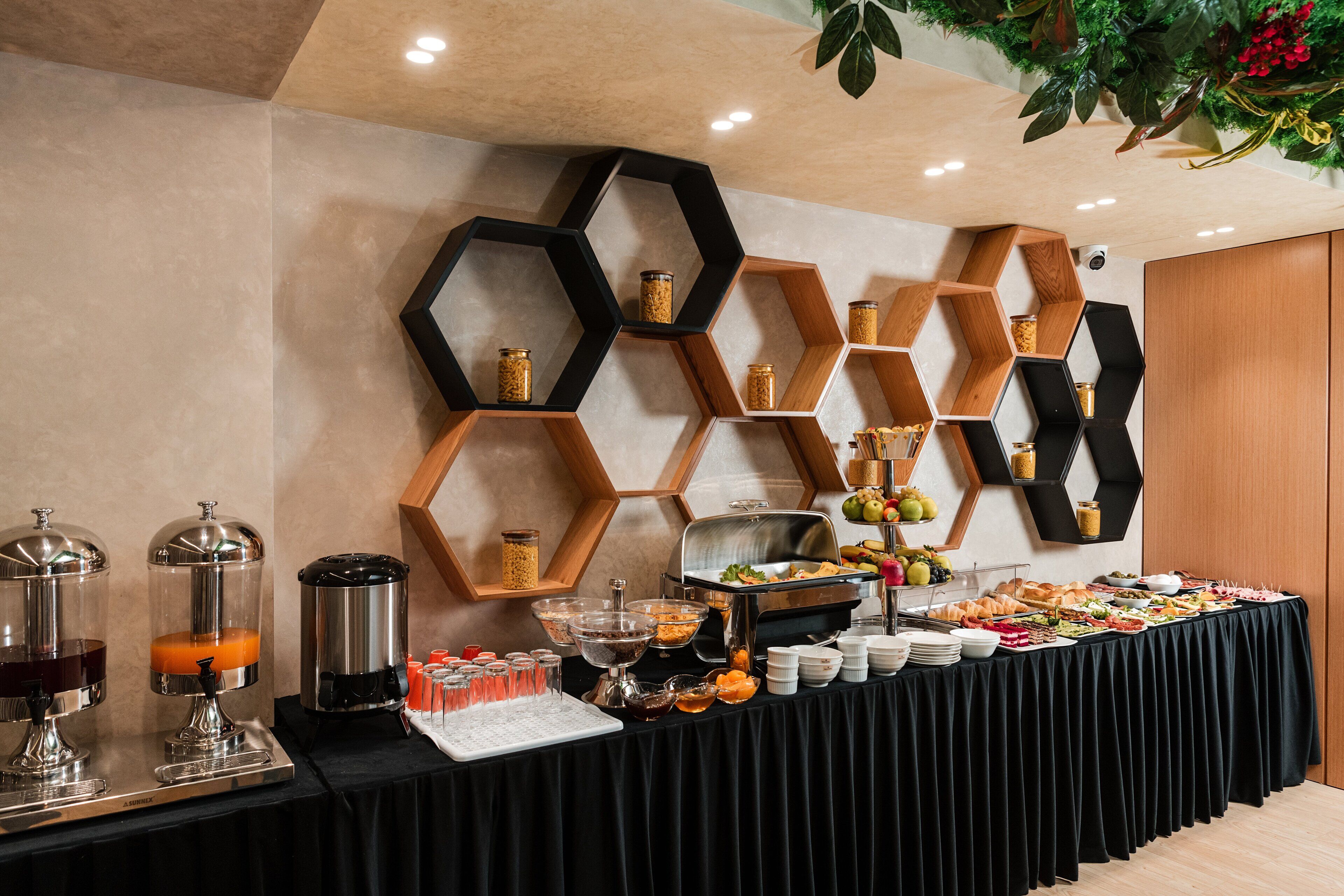 A buffet setup with various food items and beverages, including a coffee machine, fruit bowls, and a variety of dishes on a table covered with a black cloth.