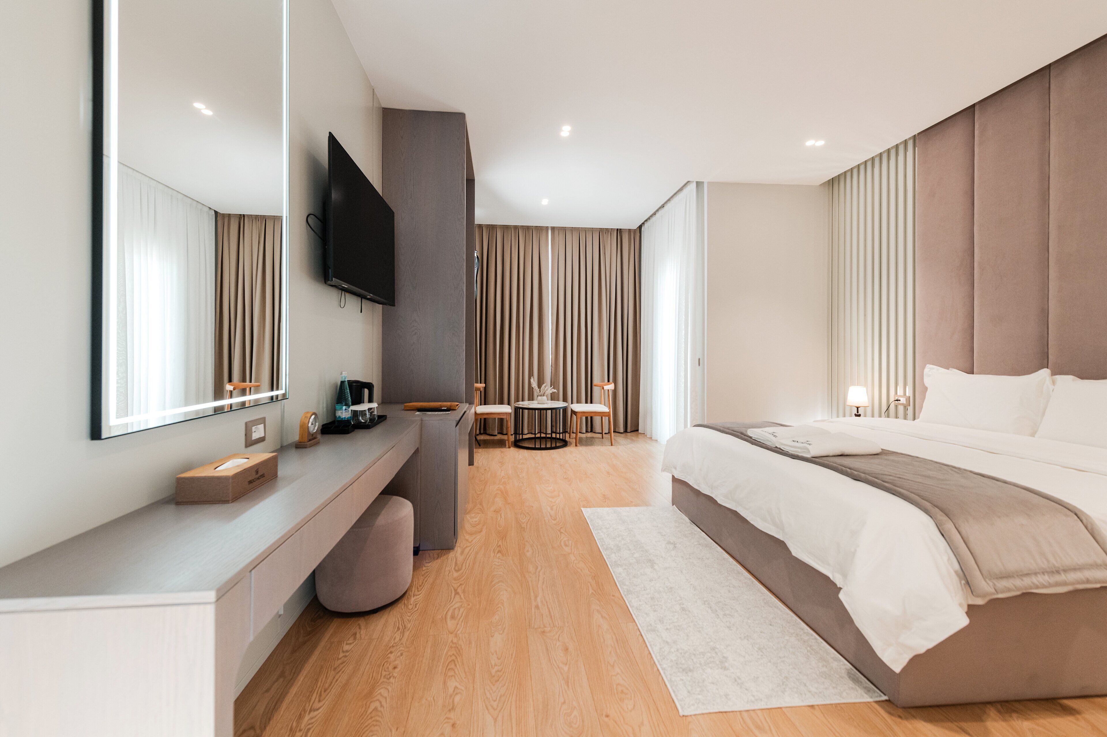 Una habitación de hotel moderna con una cama grande, un escritorio con televisor de pantalla plana, una mesa redonda con sillas y un espejo amplio.