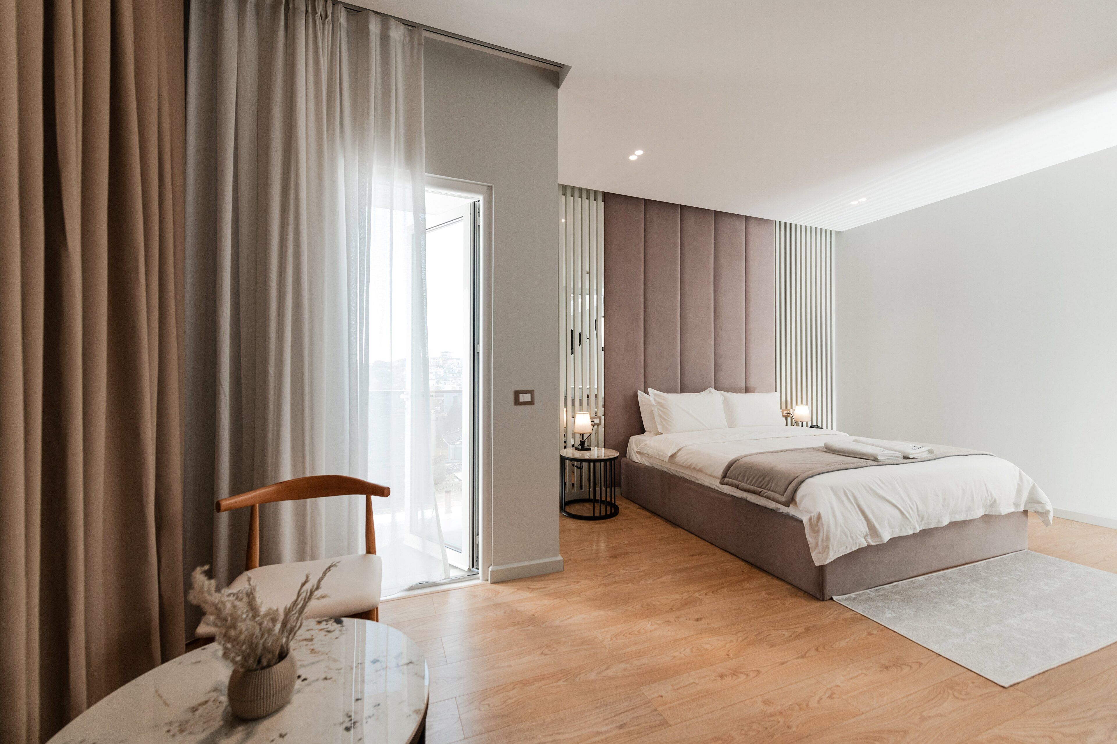 Un dormitorio moderno con una cama grande, una mesita de noche con lámpara y vistas a la ciudad a través de un ventanal.