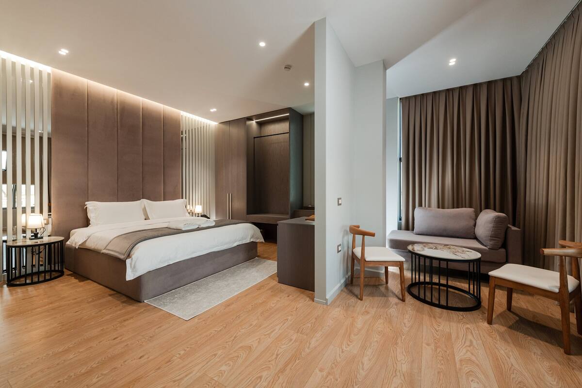 A modern bedroom with a large bed, a seating area with a sofa and chairs, and a small table.