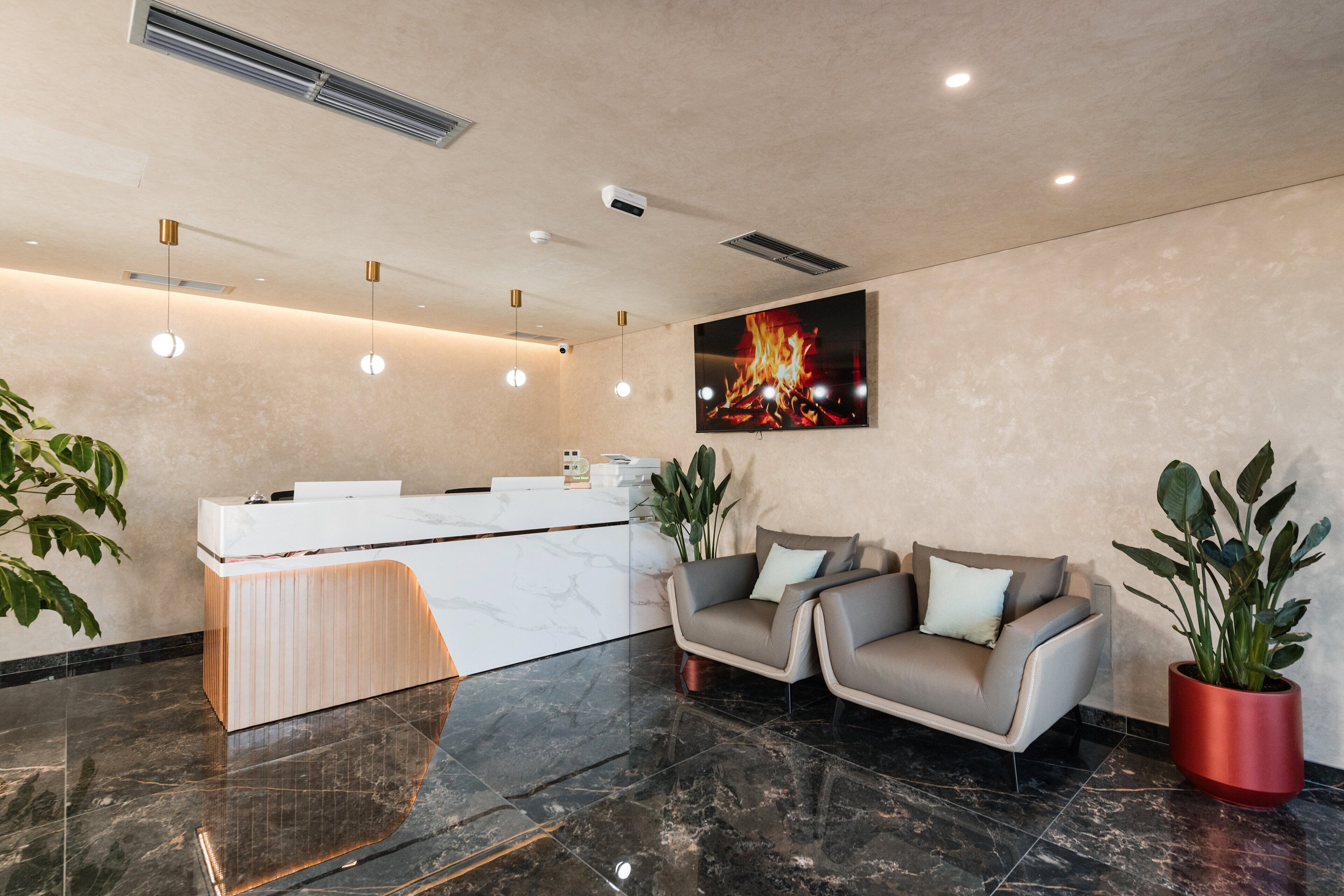 A modern reception area with a marble reception desk, two sofas, and a large painting of a fire.