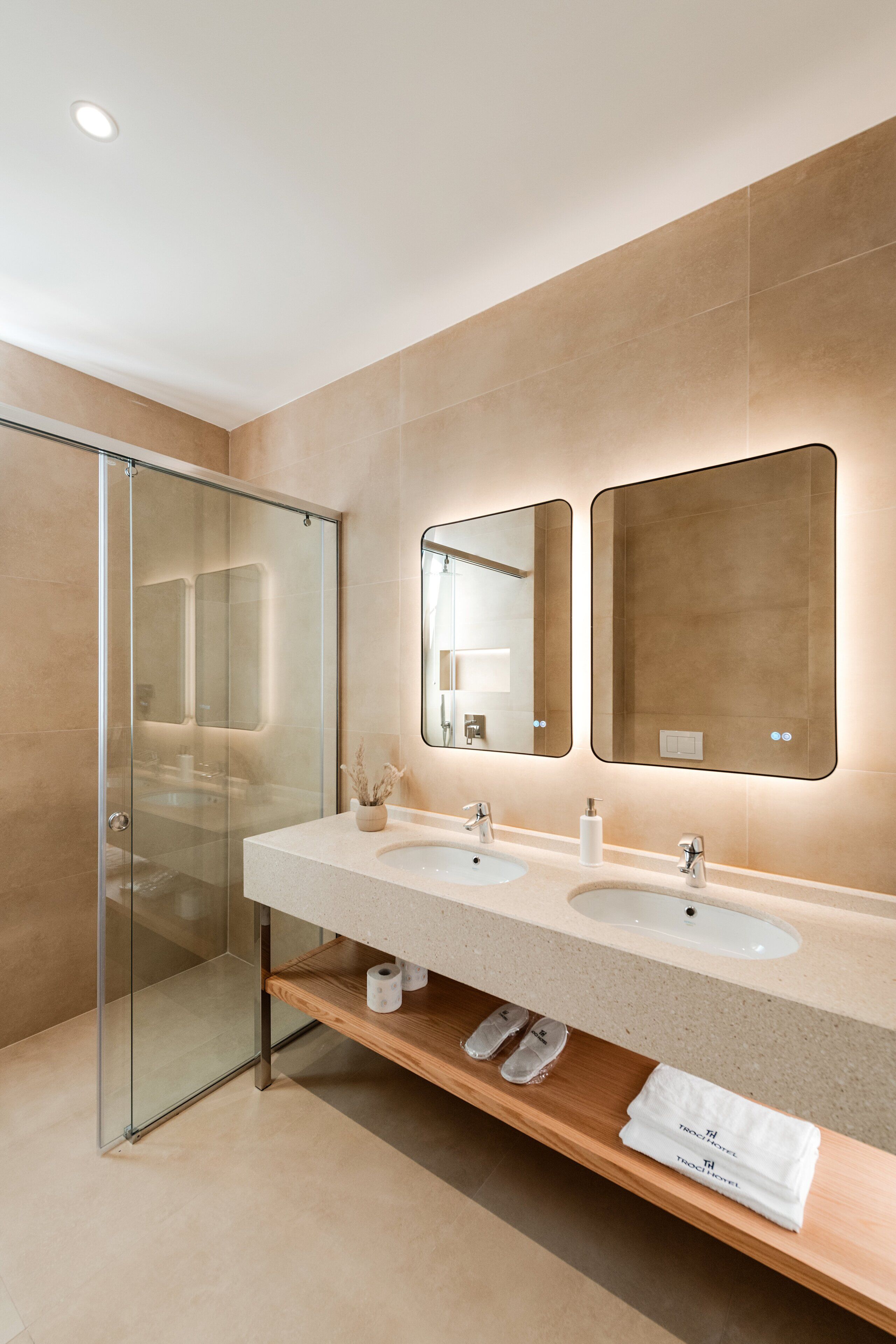 A modern bathroom with a glass shower enclosure, two sinks, and a mirror above each sink.