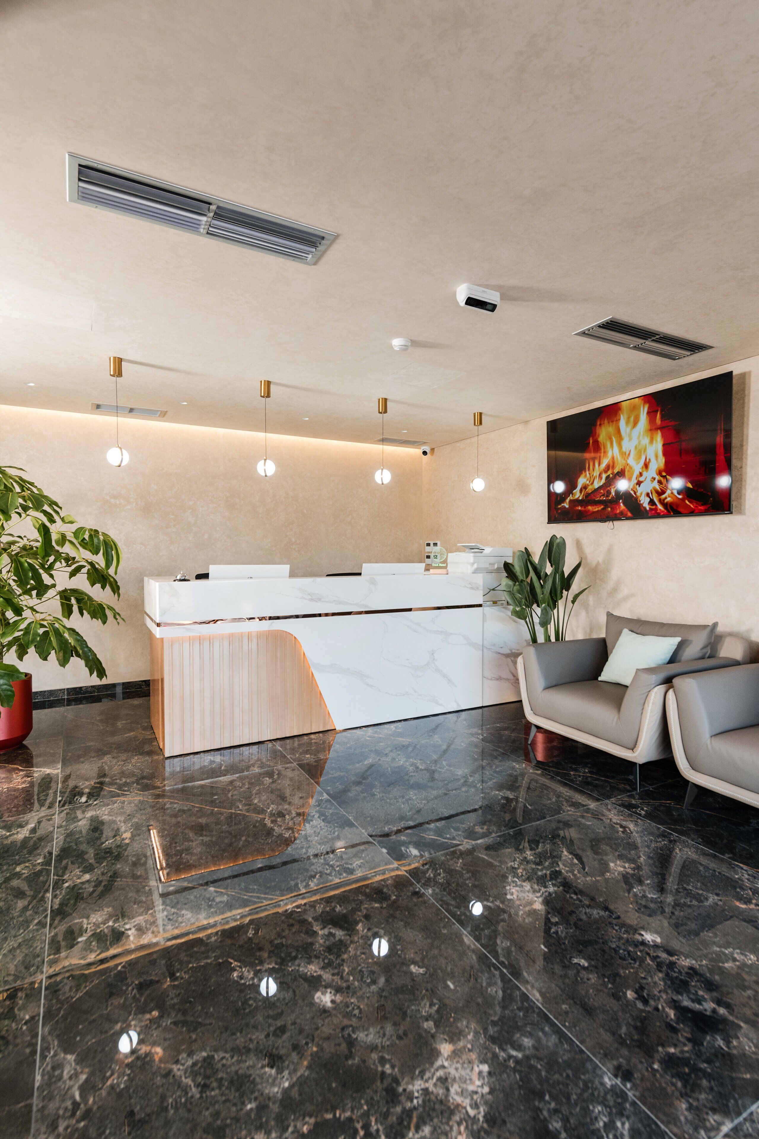 A modern reception area with a marble reception desk, a large painting of a fire, and a seating area with a grey sofa.