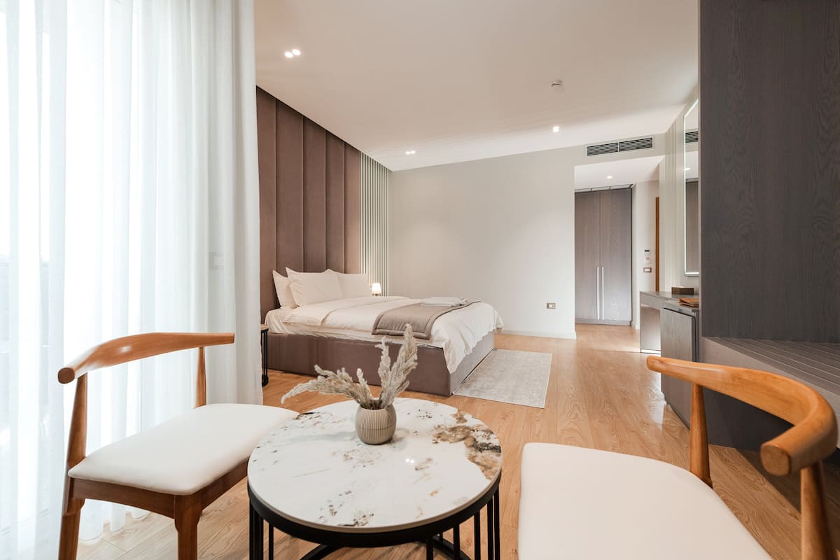A modern bedroom with a bed, bedside tables, and a view into the adjacent kitchen.