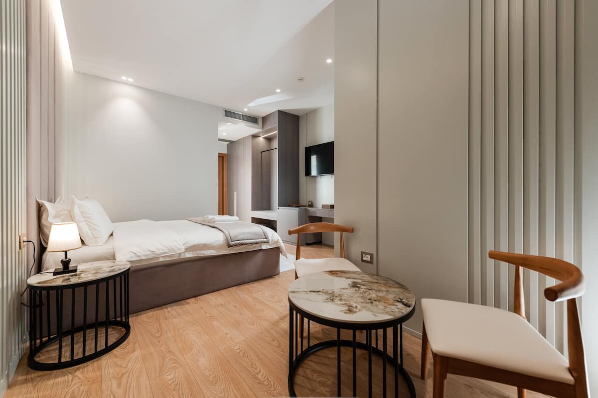 A modern hotel room with a bed, bedside table, lamp, and a small round table with a chair.