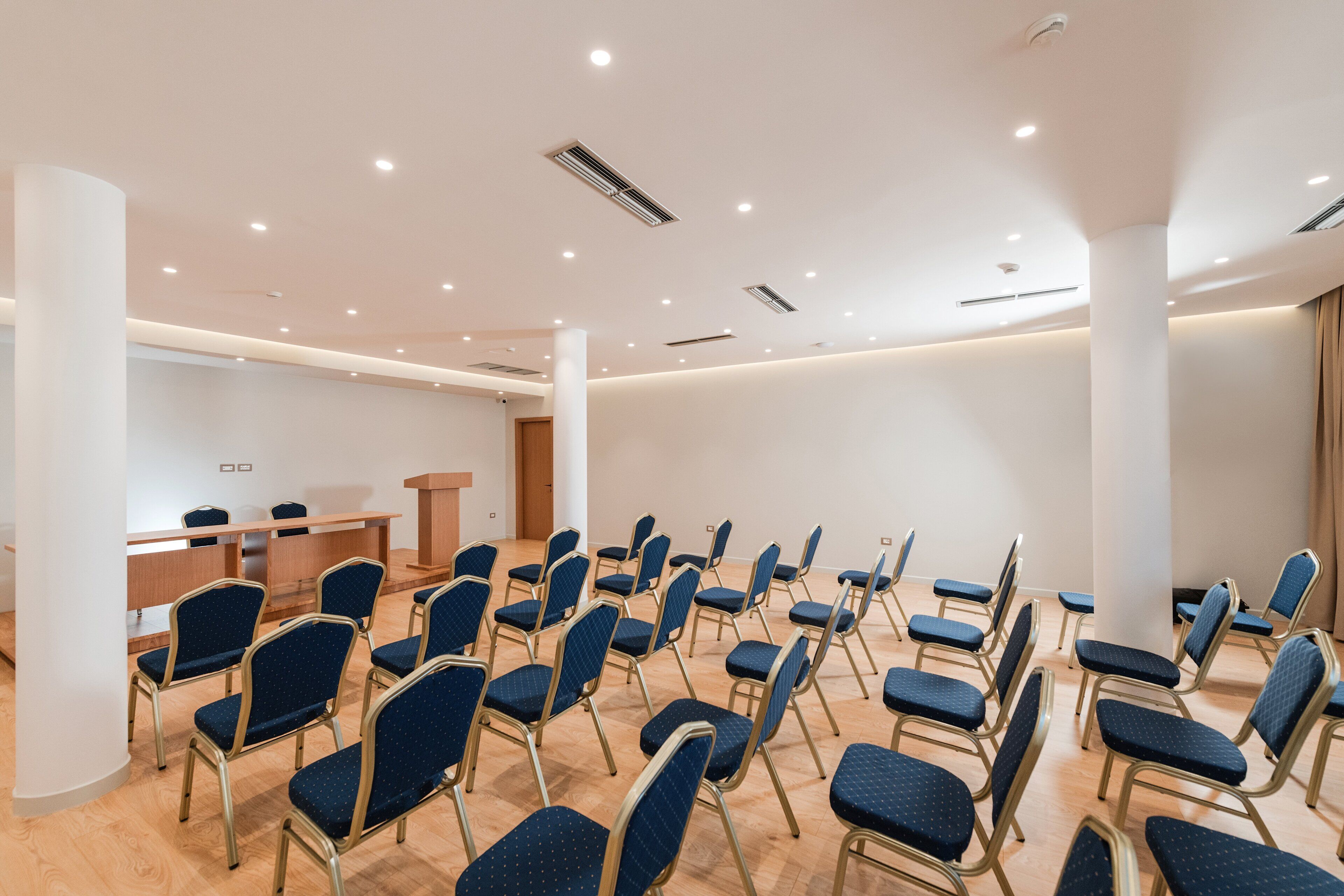 A conference room with rows of blue chairs, a podium, and a wooden desk.