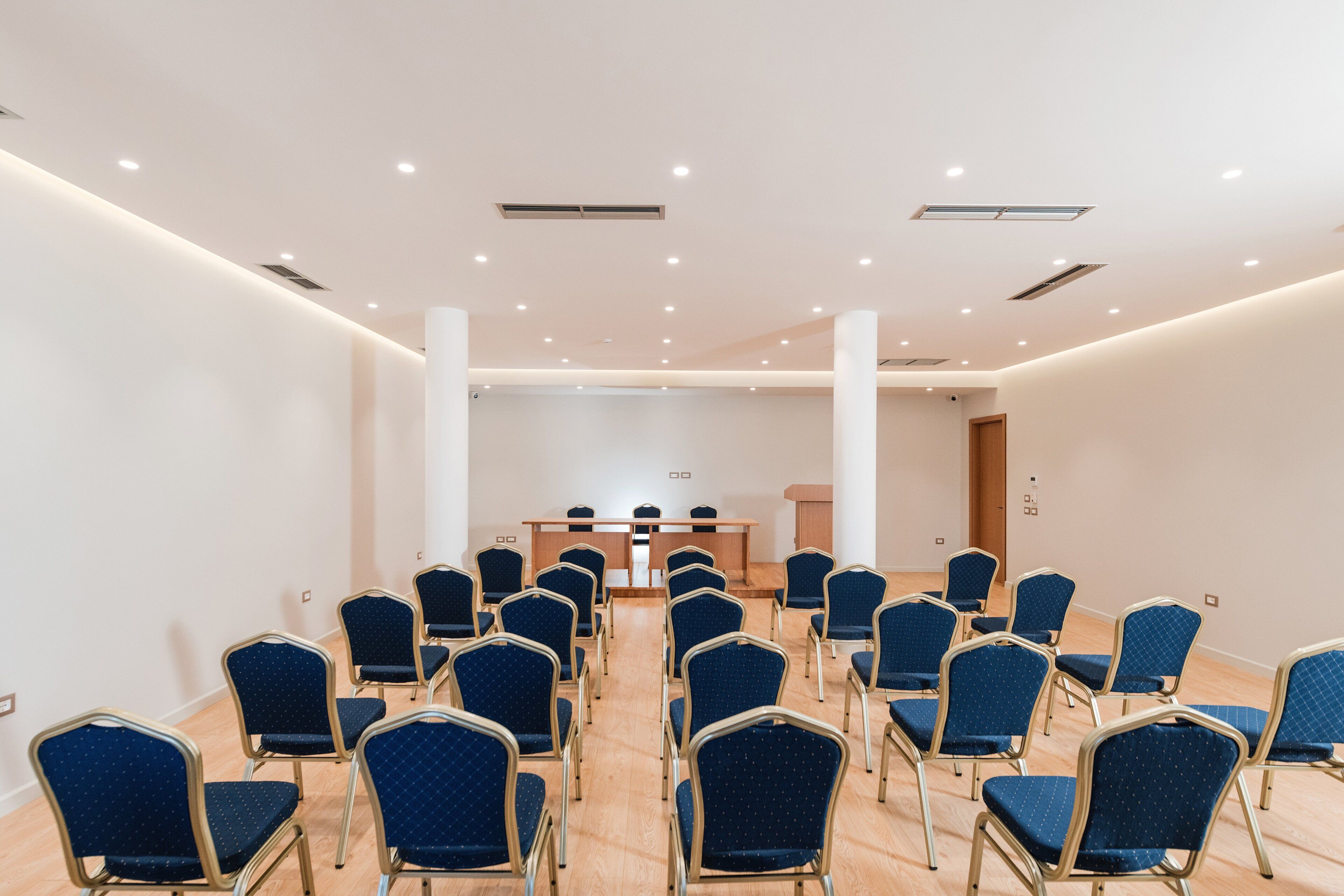 A conference room with rows of blue chairs, a wooden table, and a podium.