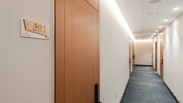 A hotel corridor with wooden doors, a blue carpet, and a sign indicating room number 301.