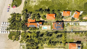An aerial view of a resort with multiple buildings, palm trees, a swimming pool, and beach umbrellas. - Xaréu Flats Maragogi (Maragogi)