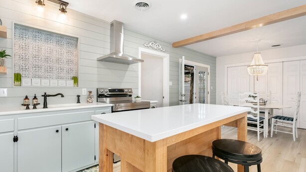 A modern kitchen with a central island, wooden accents, and a dining area with a chandelier.