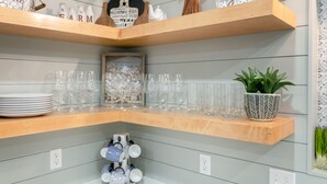 A kitchen shelf with wine bottles, glasses, and a small potted plant.
