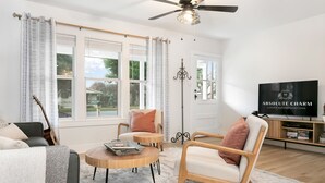 A modern living room with a round wooden coffee table, two armchairs, a sofa, a television, and a ceiling fan.