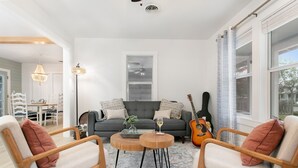 A living room with a grey sofa, two wooden armchairs, a coffee table, and a guitar.
