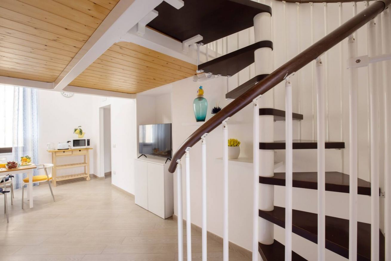 Een modern interieur met een houten plafond, een trap met witte leuningen en donkere treden, een keuken met een magnetron, een televisie en een kleine tafel met stoelen.