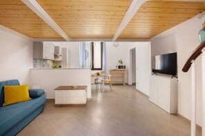 Una sala de estar moderna con techo de madera, un sofá con cojines amarillos, una zona de comedor con mesa y sillas, y un televisor sobre un mueble.