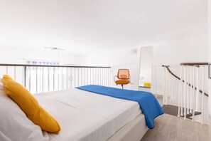 Habitación de hotel con cama, una silla, una manta azul, almohada blanca, un espejo y una escalera.