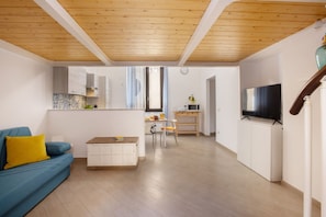 A modern living room with a wooden ceiling, a sofa with yellow cushions, a dining area with a table and chairs, and a TV on a cabinet.