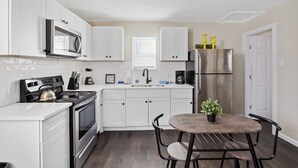A modern kitchen with white cabinets, stainless steel appliances, a dining table with chairs, and a potted plant.