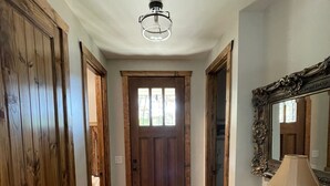 Ein Flur mit Holzböden, einer Tür mit Fenster, einem Spiegel und einem Schreibtisch mit Lampe.