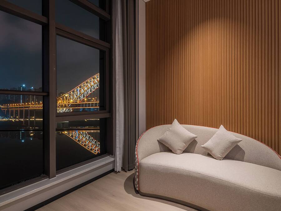 Ein modernes Wohnzimmer mit einer Couch, einem großen Fenster mit Blick auf eine beleuchtete Brücke und einer Holzwand.