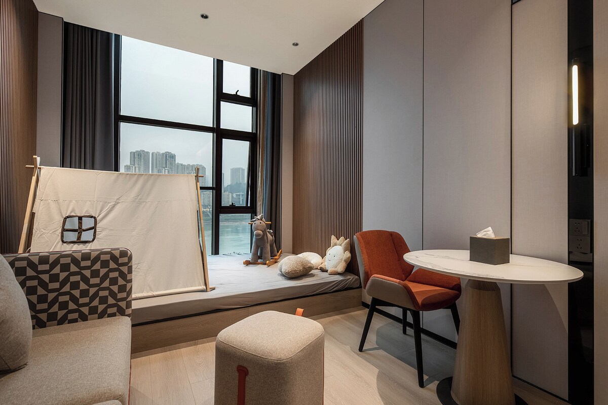 A modern hotel room with a large window, a bed with a view, a small table, and a sofa.