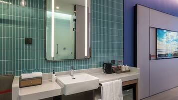 A modern bathroom with a dual sink vanity, a large mirror, and a wall-mounted television.