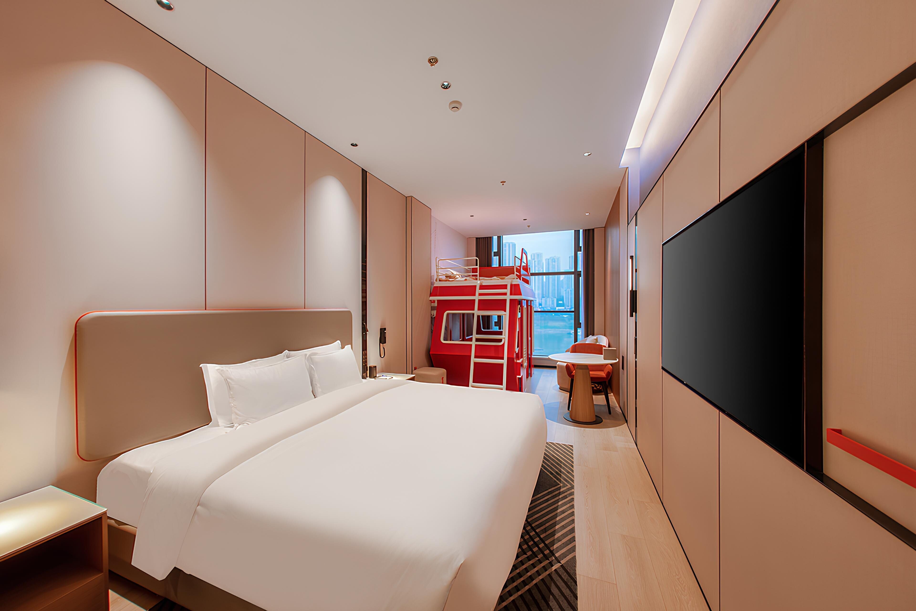 A modern hotel room with a large bed, a TV, and a view of the city.