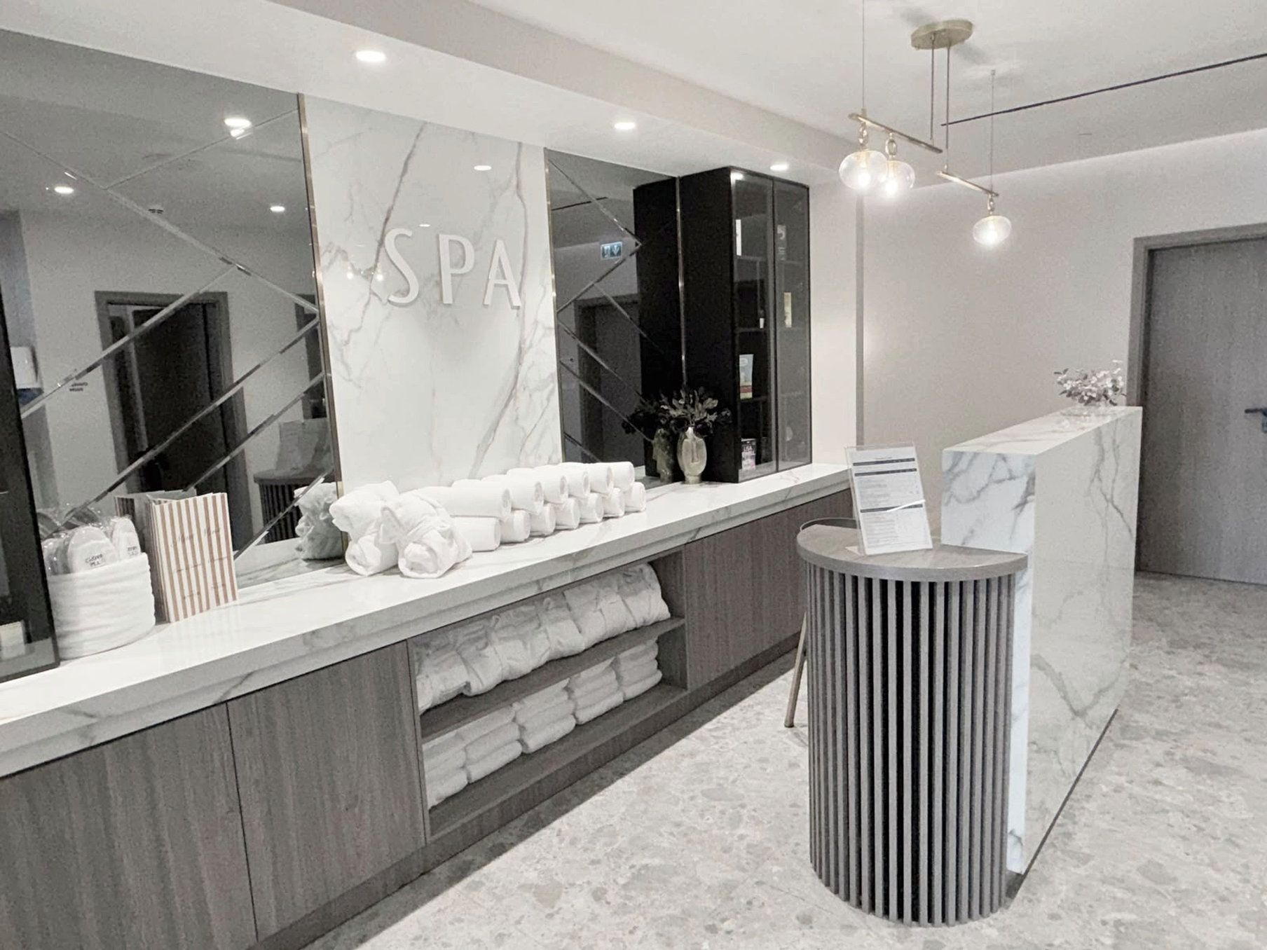 A modern spa reception area with a marble countertop, a large mirror, and a round, ribbed side table.