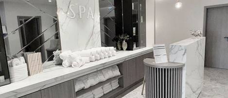 A modern spa reception area with a marble countertop, a large mirror, and a round, ribbed side table.