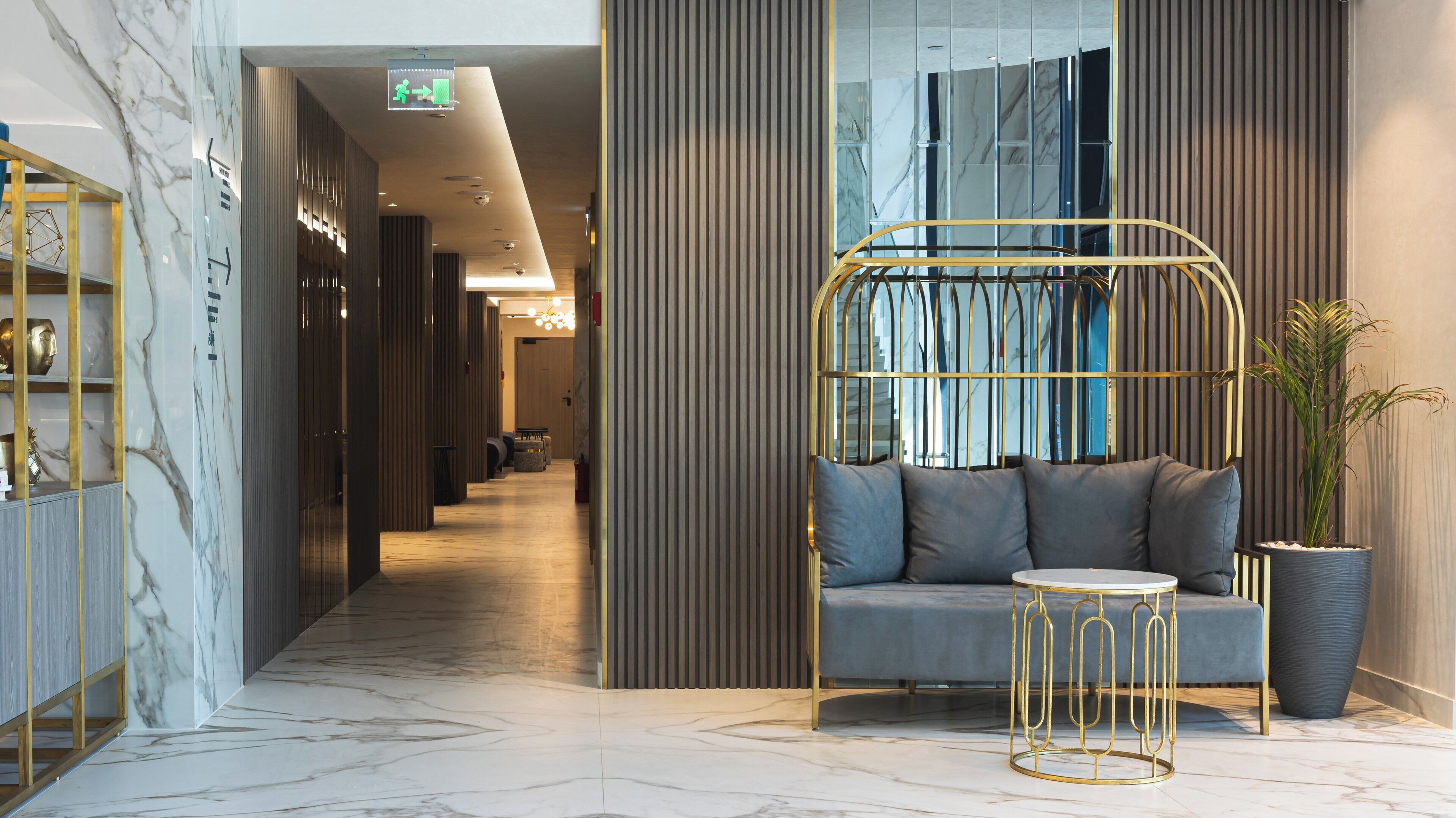 Eine moderne Lobby mit Marmorboden, einer Couch mit Kissen, einem runden goldenen Tisch und einer Kübelpflanze.