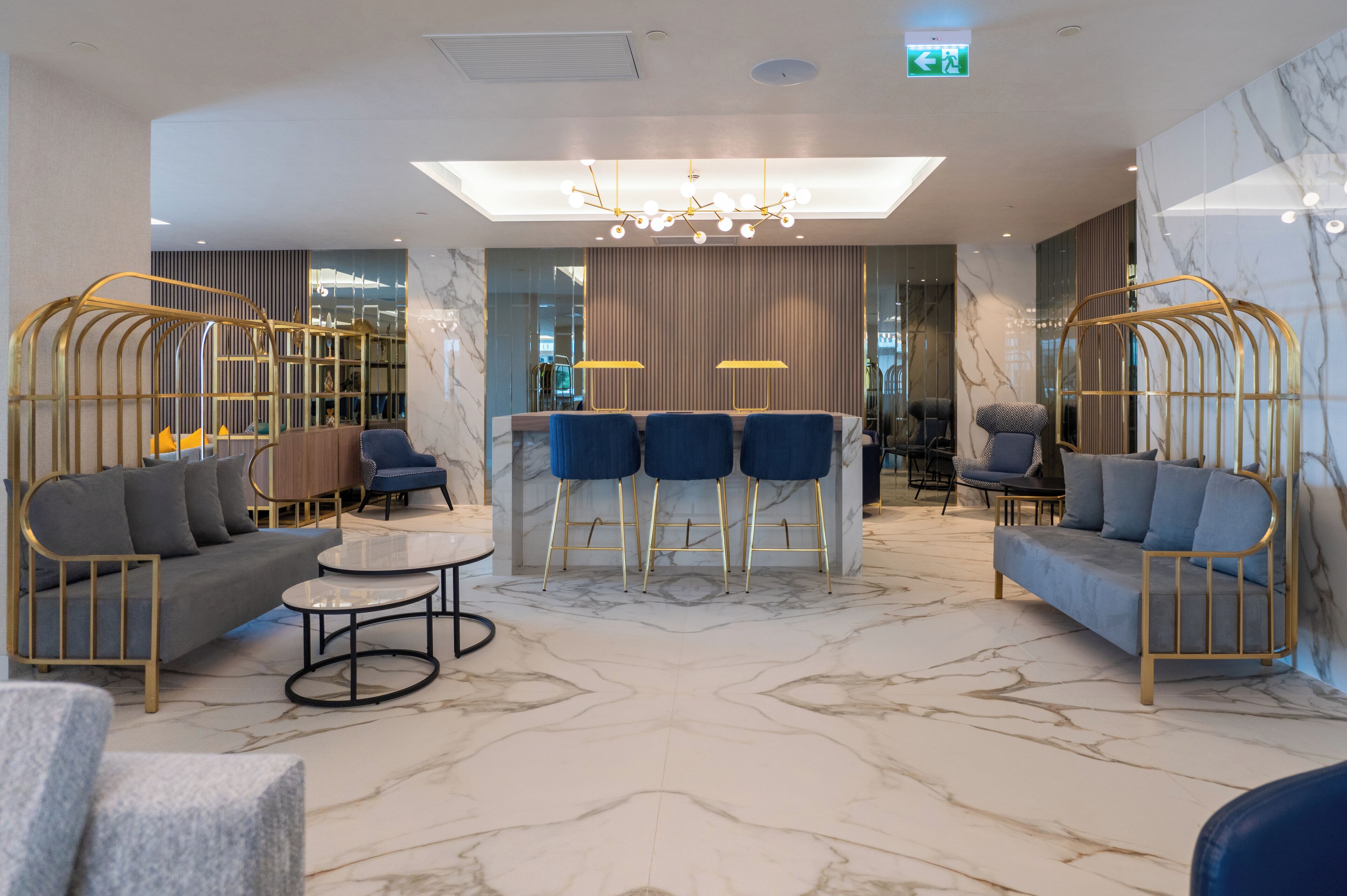 Un vestíbulo de hotel moderno con suelo de mármol, una zona de bar central y diferentes disposiciones de asientos.
