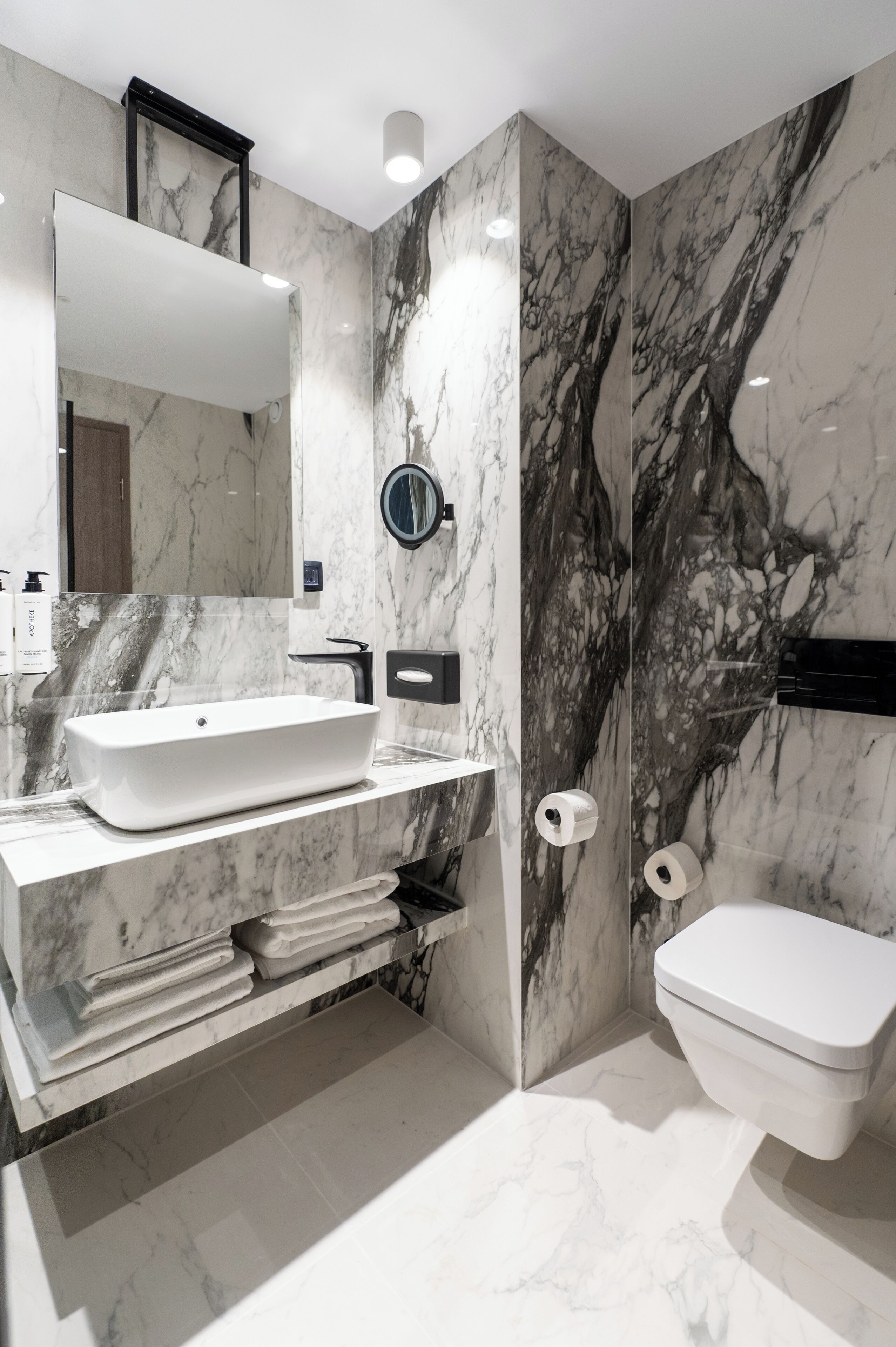 A modern bathroom with a white sink, a large mirror, and a toilet.
