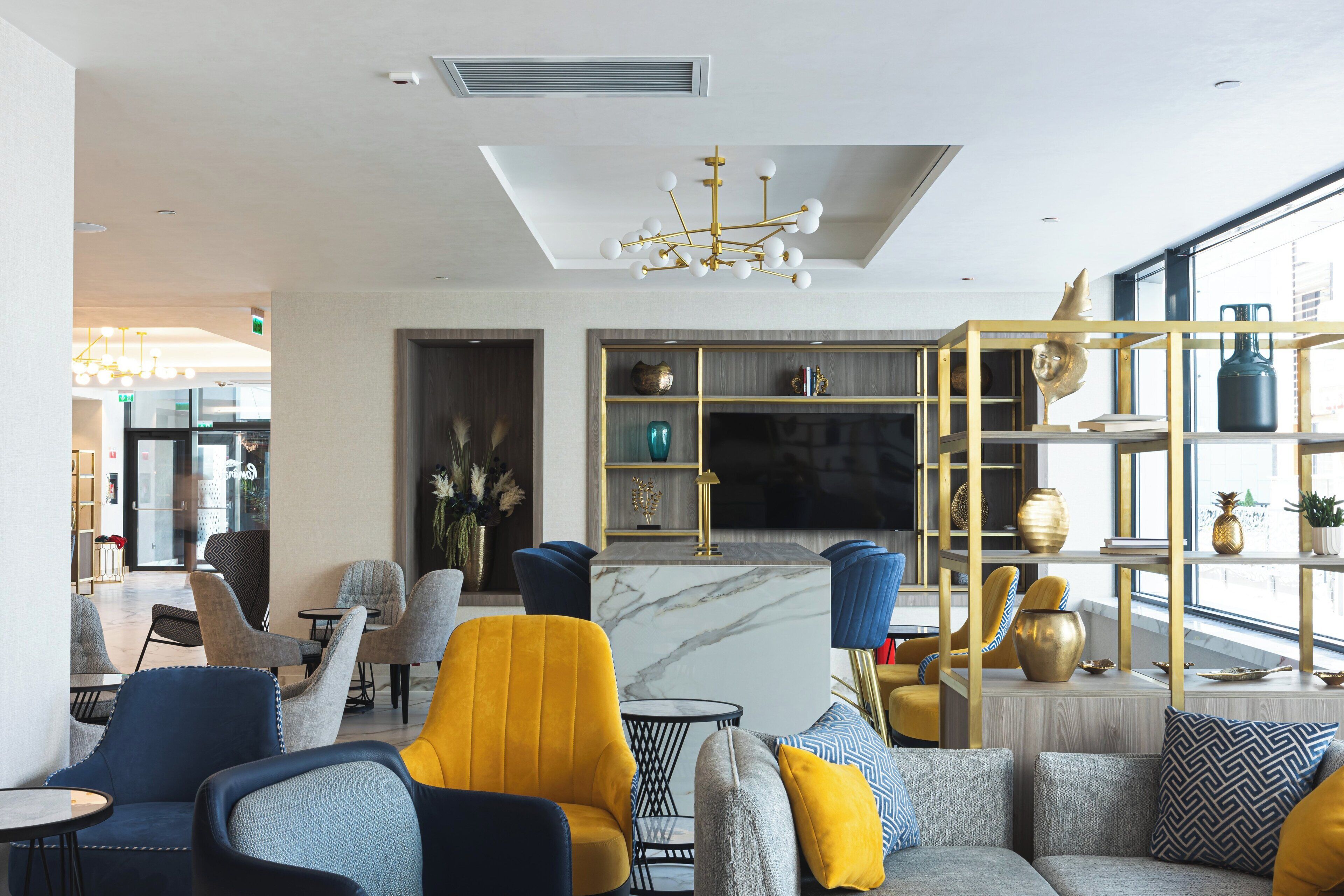 A modern hotel lobby with a seating area, a TV, and a decorative shelf with vases.