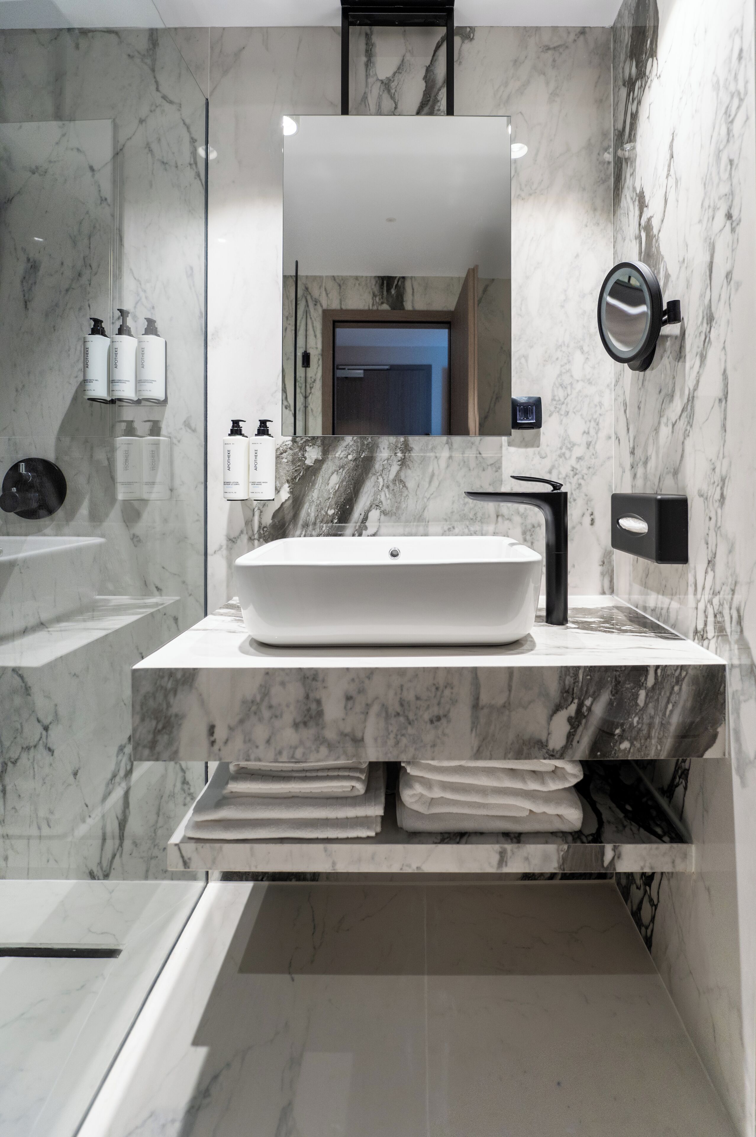 Un baño moderno con un lavamanos grande de color blanco, un grifo negro y un espejo encima. Hay artículos de tocador en la pared y un perchero debajo del lavamanos.