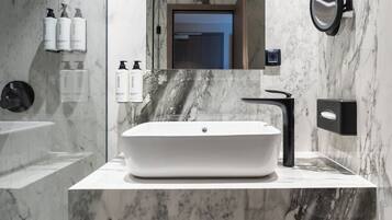 Un baño moderno con un lavamanos grande de color blanco, un grifo negro y un espejo encima. Hay artículos de tocador en la pared y un perchero debajo del lavamanos.
