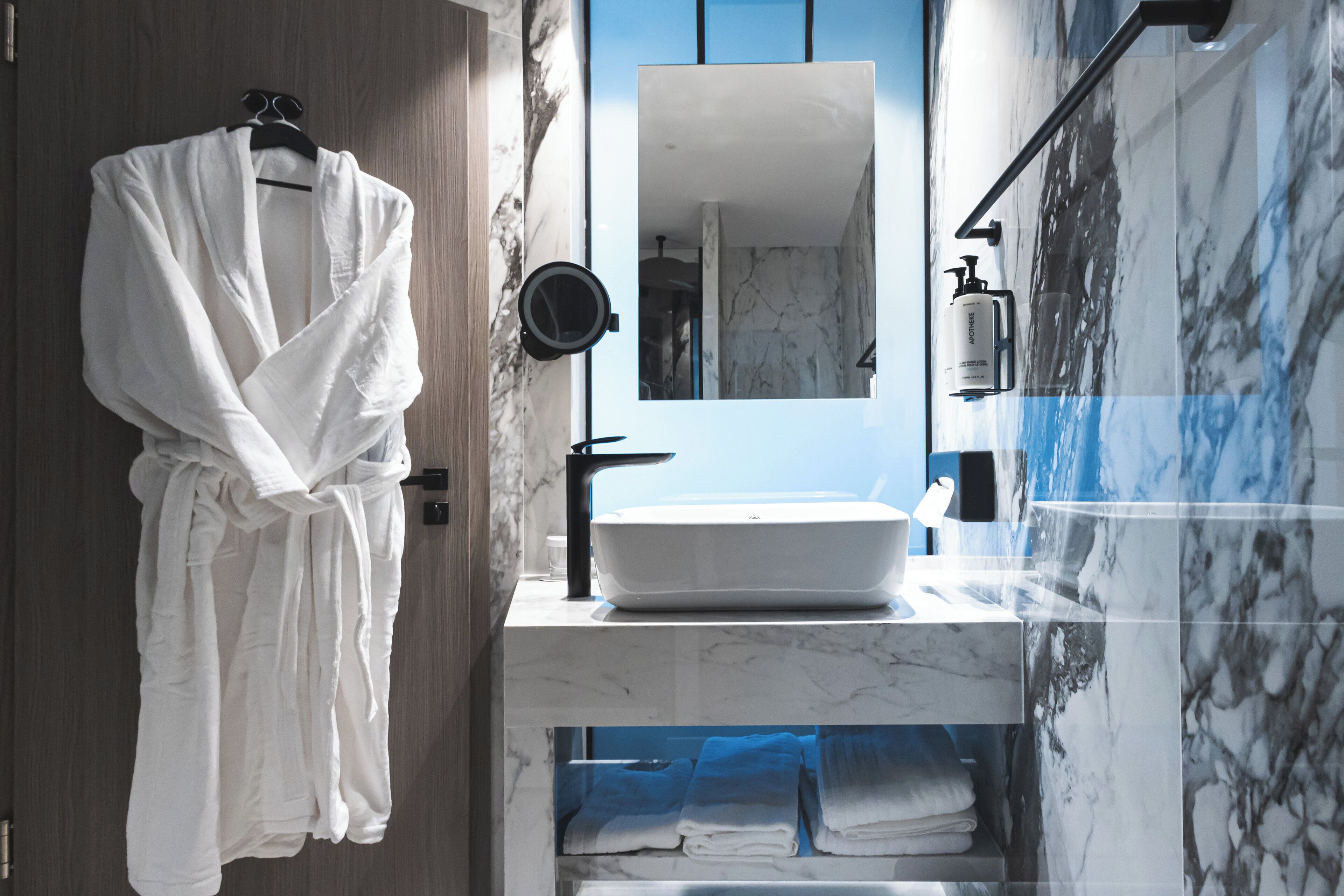Une salle de bain moderne avec un grand miroir, un lavabo blanc et un peignoir suspendu à un porte-serviettes.