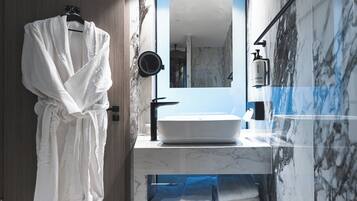 Une salle de bain moderne avec un grand miroir, un lavabo blanc et un peignoir suspendu à un porte-serviettes.