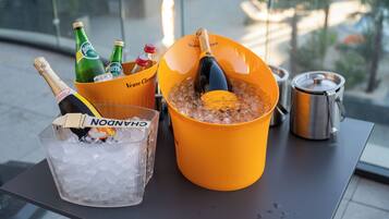 A table with a large yellow bucket containing a bottle of champagne, a bottle of Perrier, and a bottle of Cointreau. There is also a clear plastic bucket with ice and a bottle of Chandon champagne.