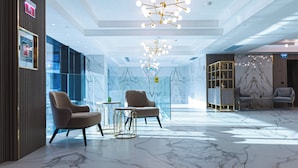 Een moderne lobby met marmeren vloeren, twee fauteuils, een bijzettafeltje en een decoratieve kroonluchter.