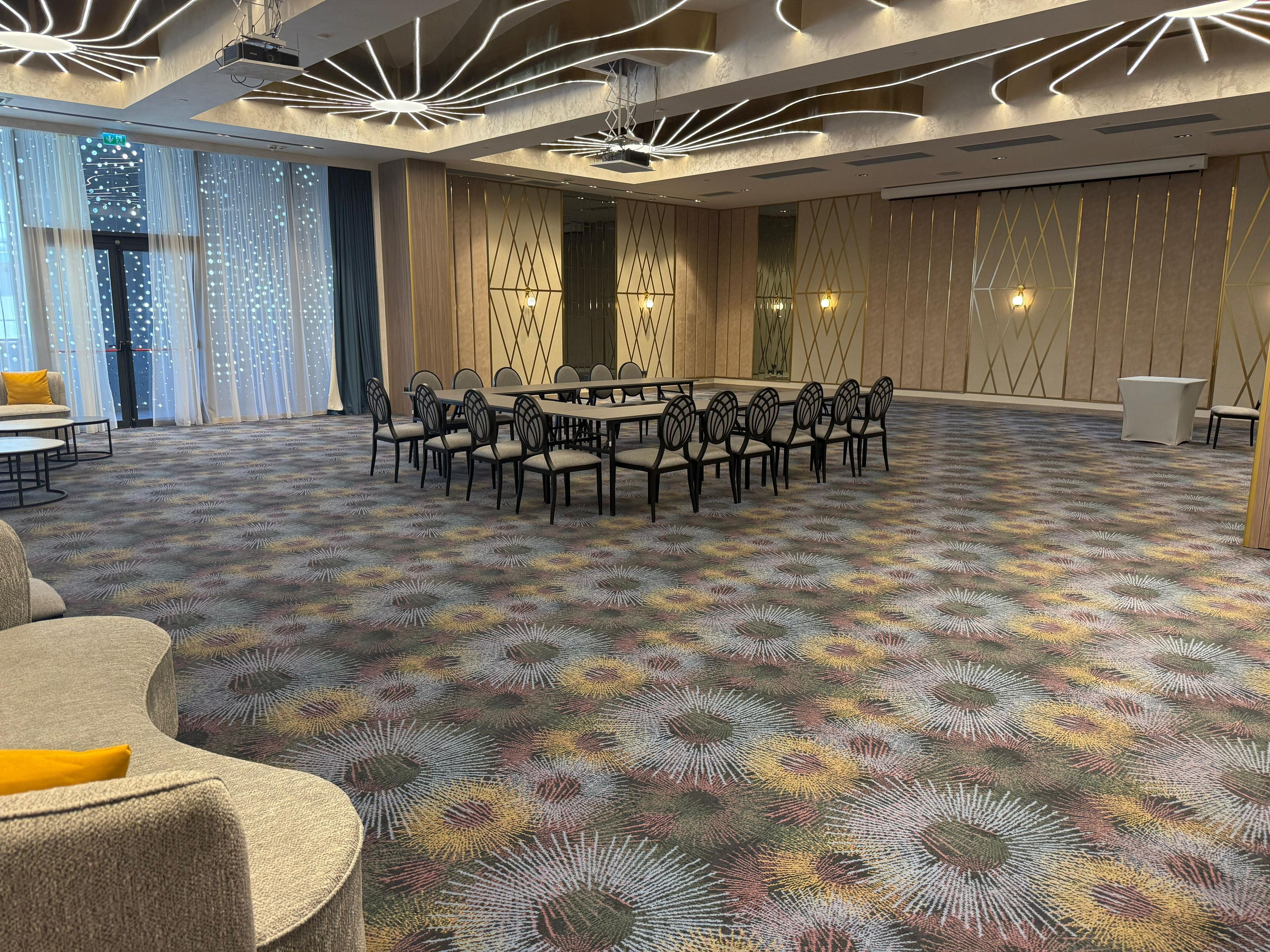 A conference room with a round table and chairs, a patterned carpet, and a modern ceiling design.
