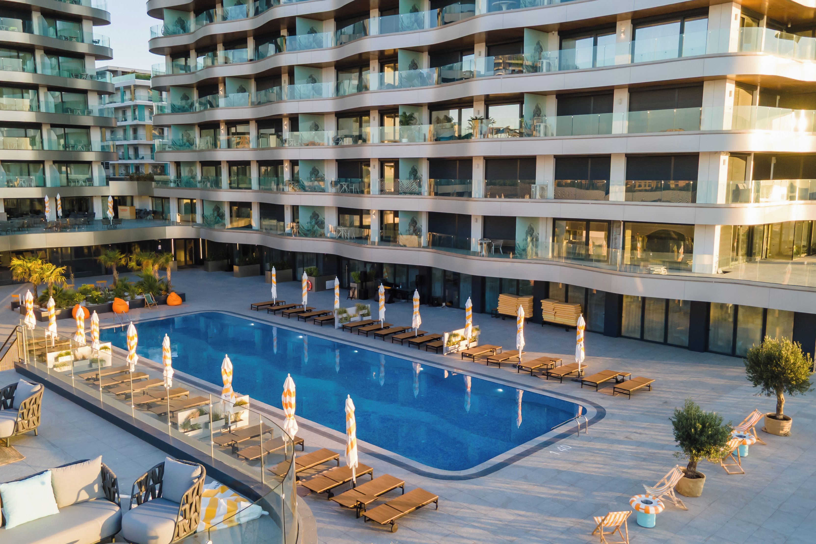 A multi-story hotel with a swimming pool, sun loungers, and outdoor seating areas.