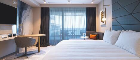 A modern hotel room with a large bed, a desk, a chair, and a television.