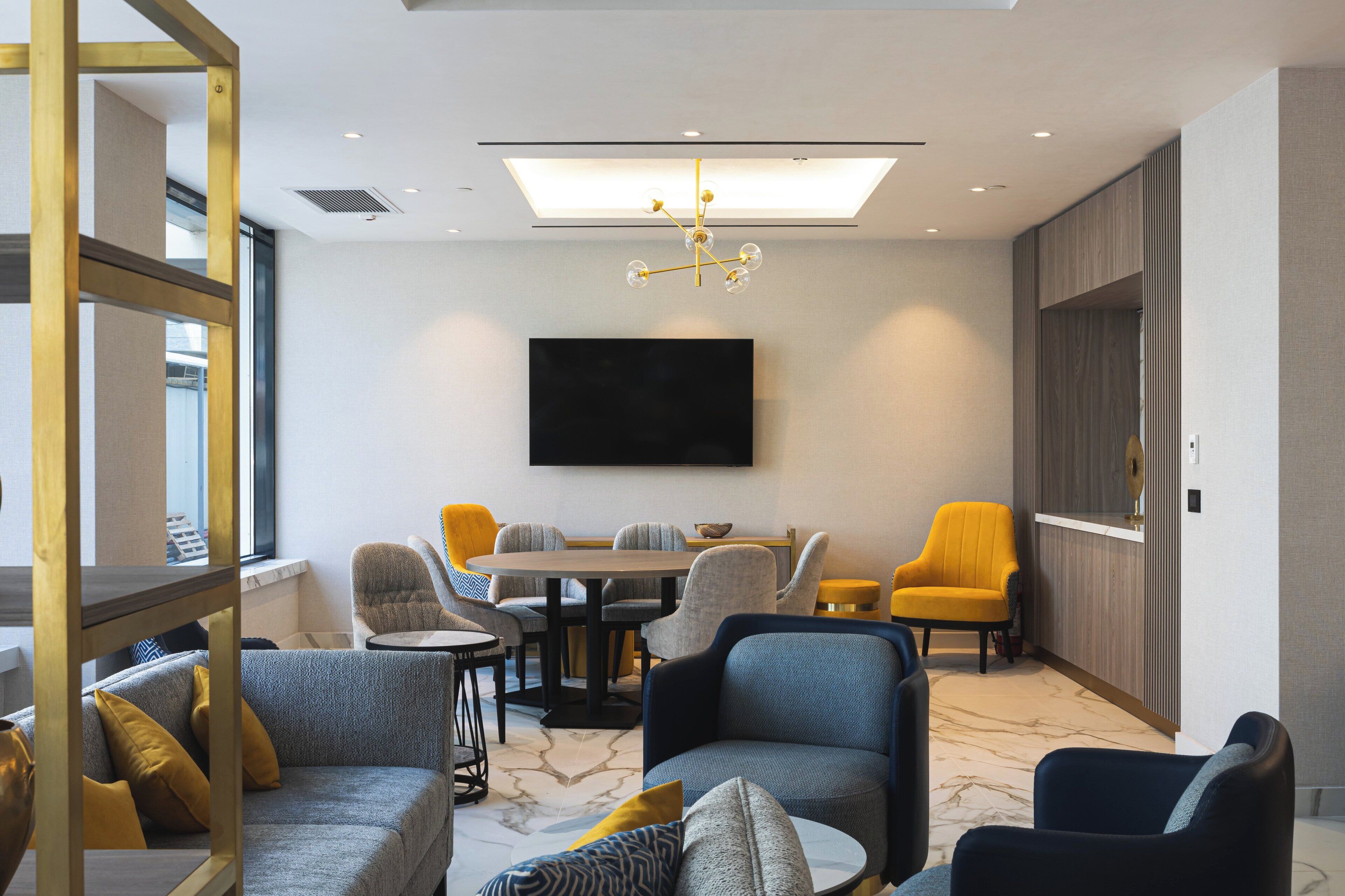 Et moderne hotelværelse med sofa, lænestole, spisebord og et fladskærms-tv monteret på væggen.