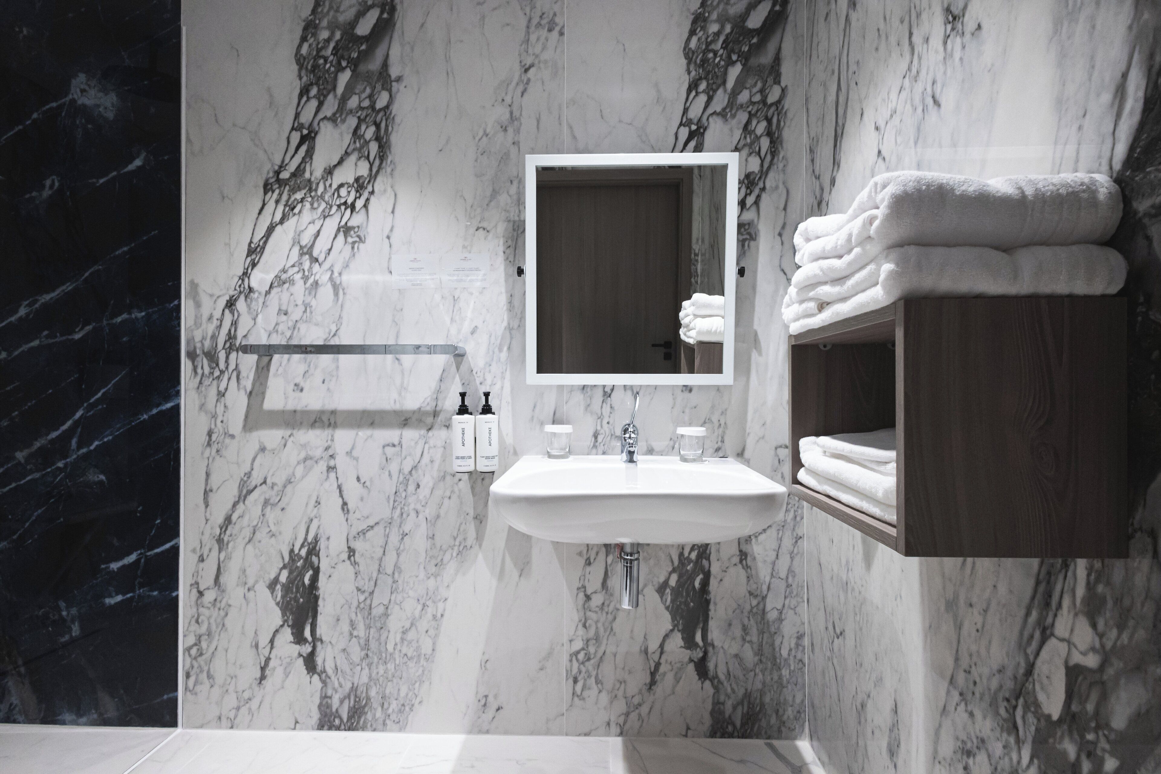 Un baño moderno con salpicadero de mármol, un lavamanos, un espejo y un perchero para toallas.