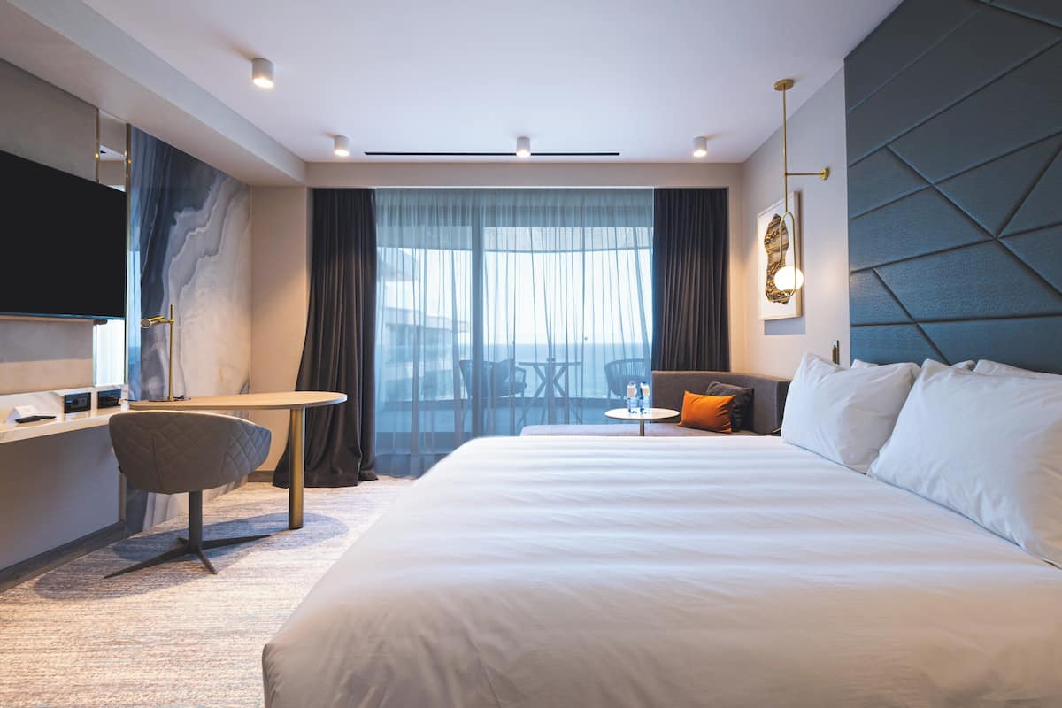Ein modernes Hotelzimmer mit einem großen Bett, einem Schreibtisch, einem Stuhl und einem Fernseher.
