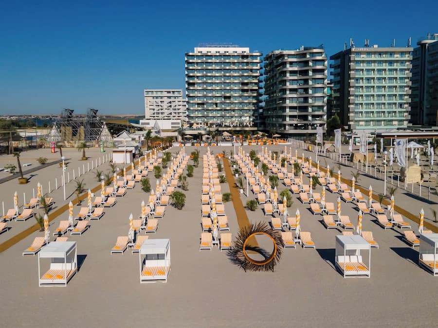 A large hotel with multiple floors, a central courtyard with numerous sun loungers and umbrellas, and a clear view of the surrounding area.