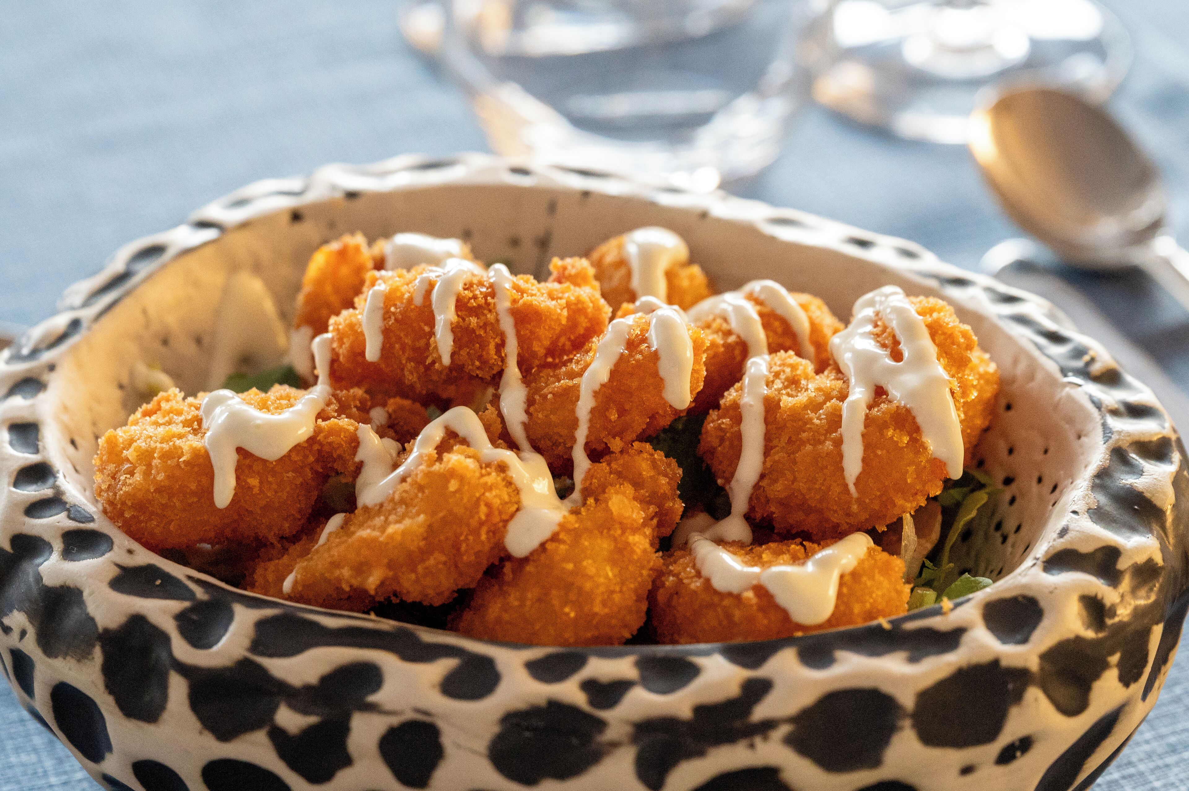 A bowl of breaded and fried food items with a creamy sauce, placed on a patterned plate.